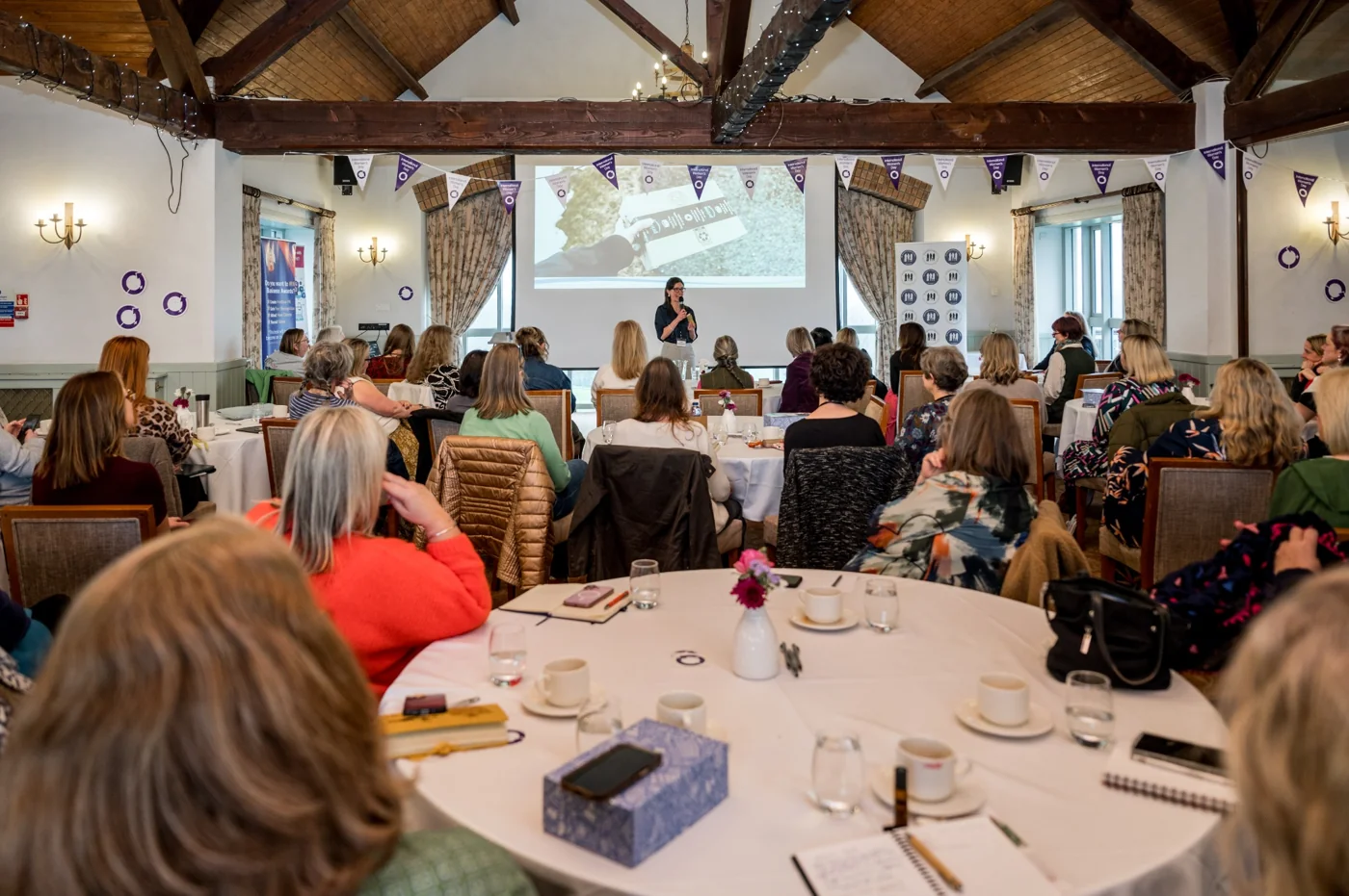 Sally speaking to an audience seated around tables